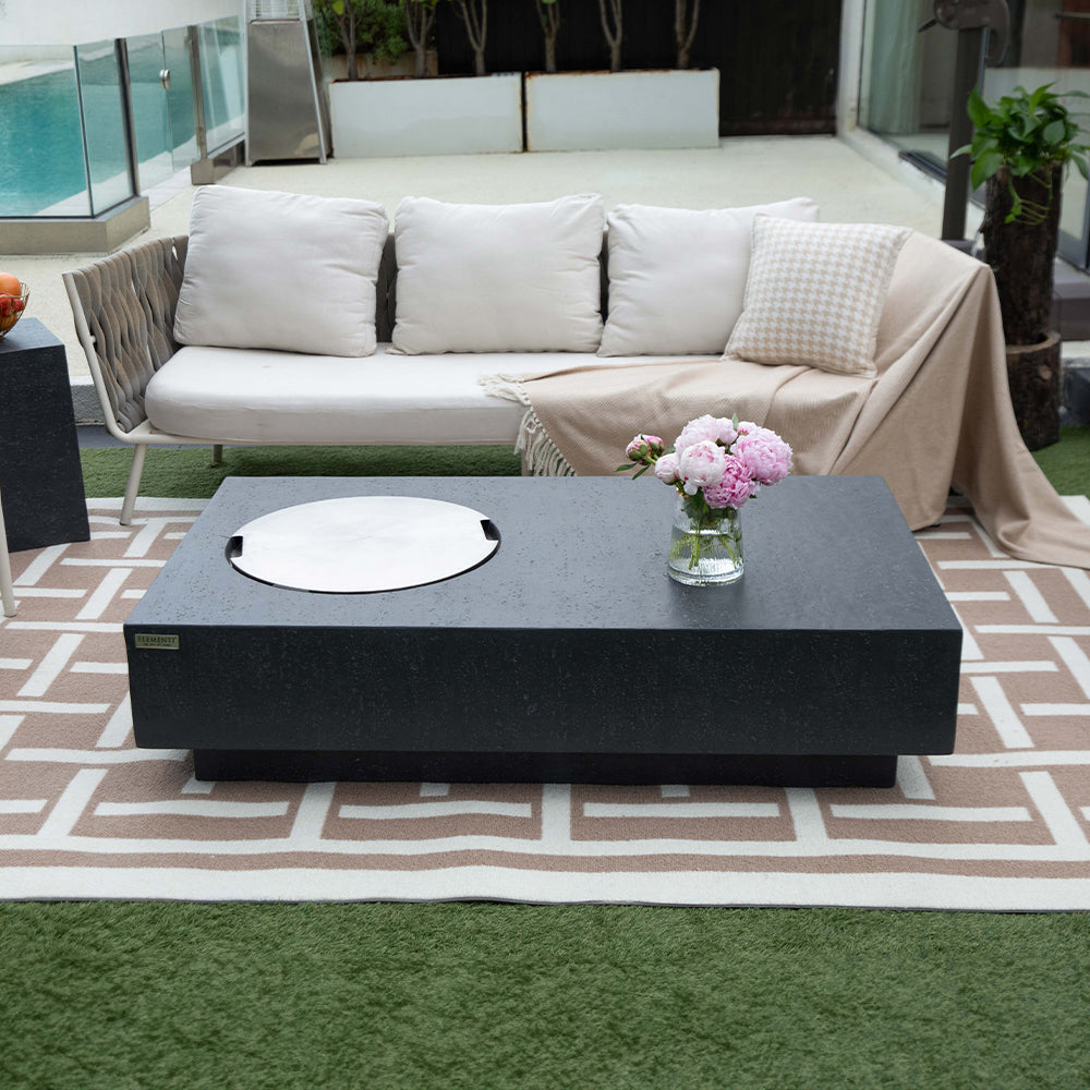 Dark grey stone fire pit table with circular burner, on patterned rug outdoors