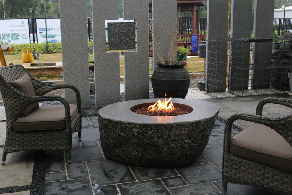 Circular stone firepit table with flames, surrounded by wicker chairs on stone patio