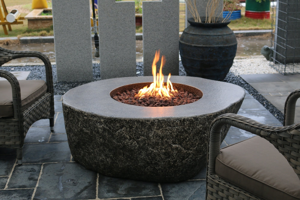 Circular stone firepit table with flames, 50 inches, on patio with wicker chairs