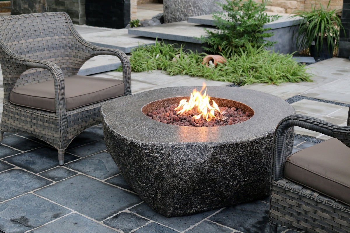Circular stone firepit with flames, surrounded by wicker chairs on stone patio