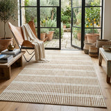 Beige and cream striped area rug on wooden floor in sunlit room with chair and potted plants