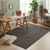 Black and beige geometric jute rug on light wood floor in a room with wooden desk and potted plant