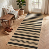 Black and beige striped jute runner rug on herringbone wood floor near bench and shoes
