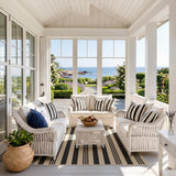 Black and beige striped jute rug on a porch with white wicker furniture and ocean view