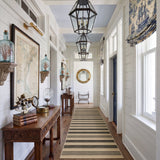Striped jute runner rug in beige and dark brown, shown in a hallway with wooden floors and white walls