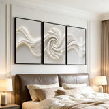 Three black-framed abstract canvas artworks with 3D textured swirls mounted above a bed in a bedroom
