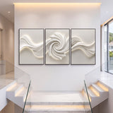 Three black-framed abstract canvas panels with white 3D textured swirls, mounted on a wall above a staircase