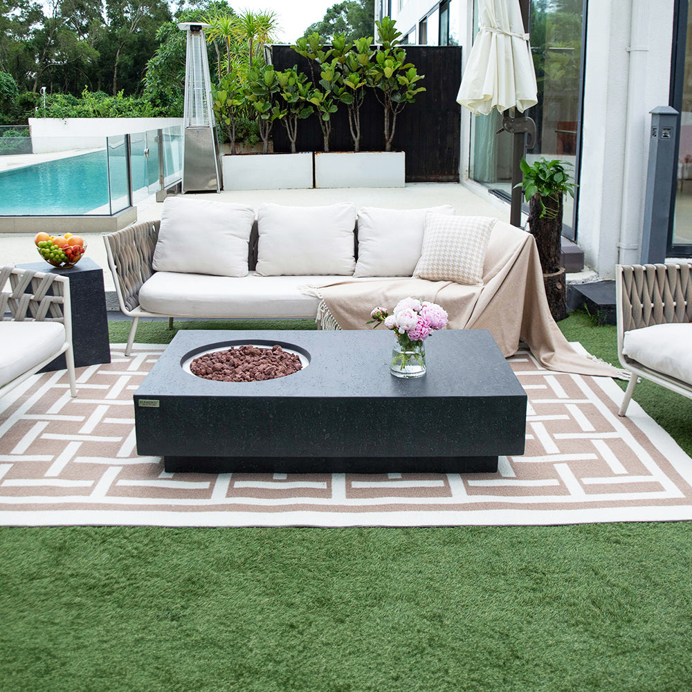 Dark grey rectangular fire pit table with circular burner, on patterned rug outdoors near sofa
