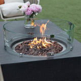 Dark grey fire pit table with glass surround and flames, outdoors on grass near patio furniture