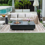 Dark grey rectangular fire pit table with glass enclosure and flames, on patio with sofa and rug