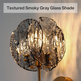 Close-up of brass wall sconce with textured smoky gray glass shade, showing light glowing through glass