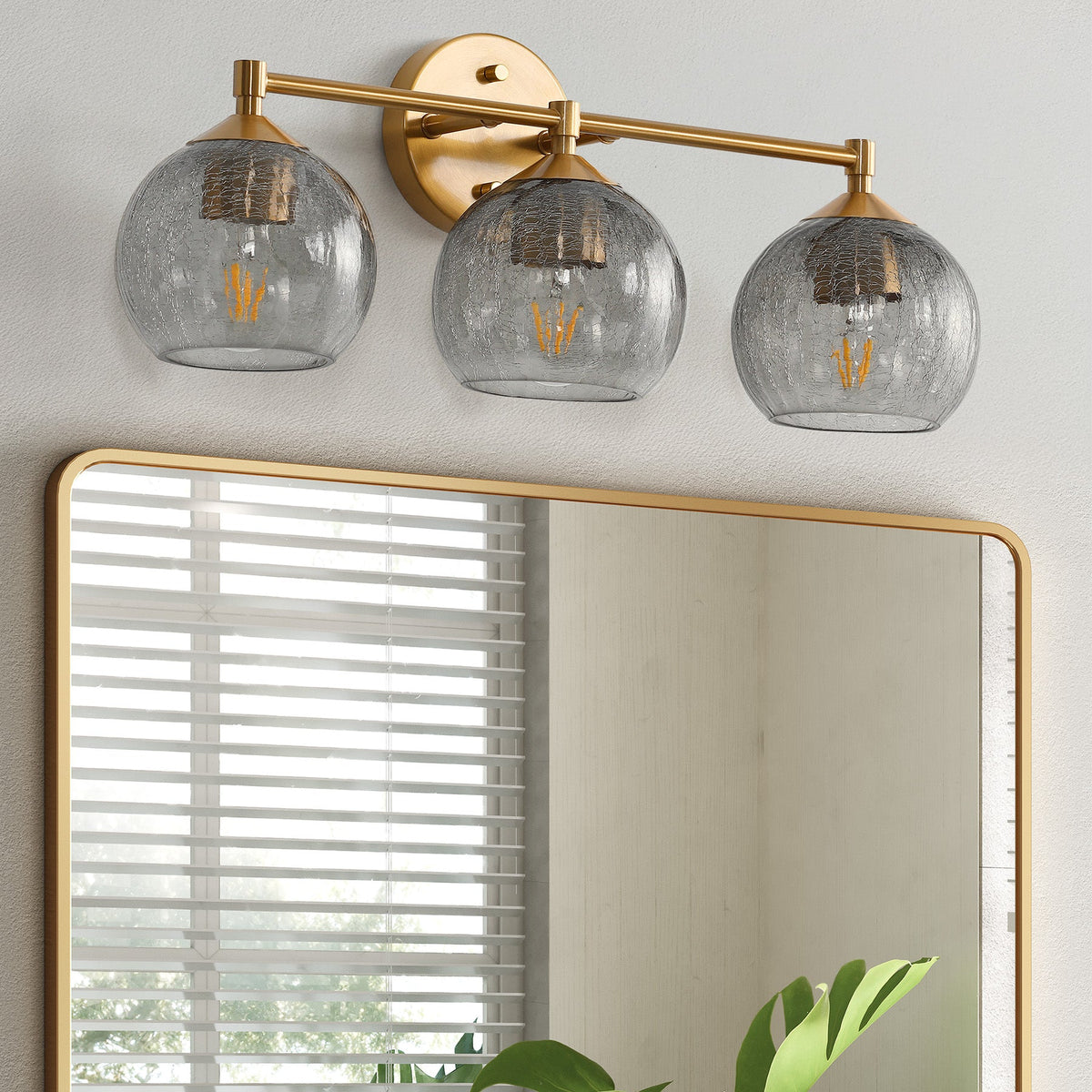 Gold bathroom vanity light with three gray crackle glass shades, shown above rectangular mirror