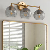 Gold bathroom vanity light with three gray crackle glass shades, shown above rectangular mirror