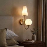 Gold double-headed wall sconce with milky white shades mounted on bedroom wall