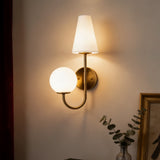 Gold double-headed wall sconce with milky white shades mounted on a wall near a curtain and framed artwork