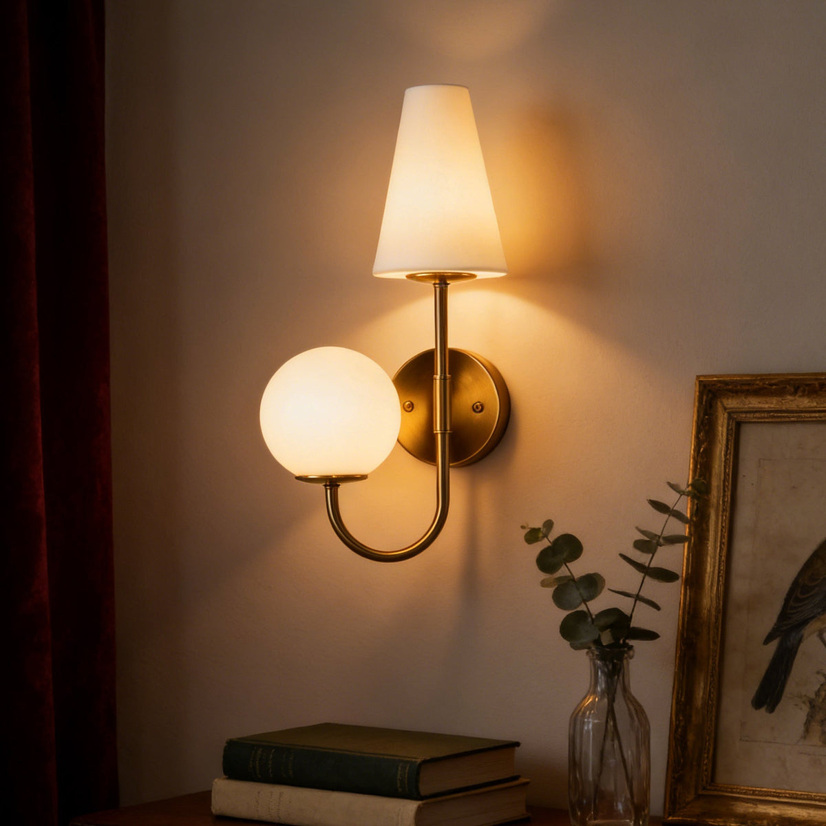 Gold double-headed wall sconce with milky white shades mounted on wall near books and framed art