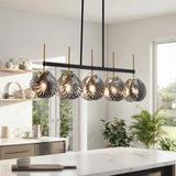 Five-light linear chandelier with smoky gray shell glass shades, black frame, and gold accents, hanging over a kitchen island