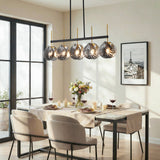 Five-light linear chandelier with smoky gray shell glass shades, black frame, and gold accents hanging over a dining table