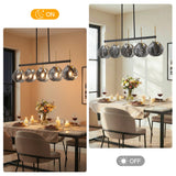 Five-light linear chandelier with smoky gray shell glass shades, black frame, and gold accents, shown lit in a dining room