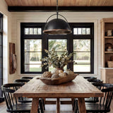 Black dome pendant light with wood trim hanging over a wooden dining table