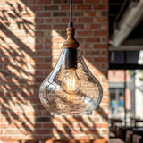 Teardrop-shaped seeded glass pendant light with wood accent, hanging against brick wall