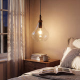 Warm farmhouse pendant light with seeded glass and wood accent hanging over a wooden nightstand in a bedroom