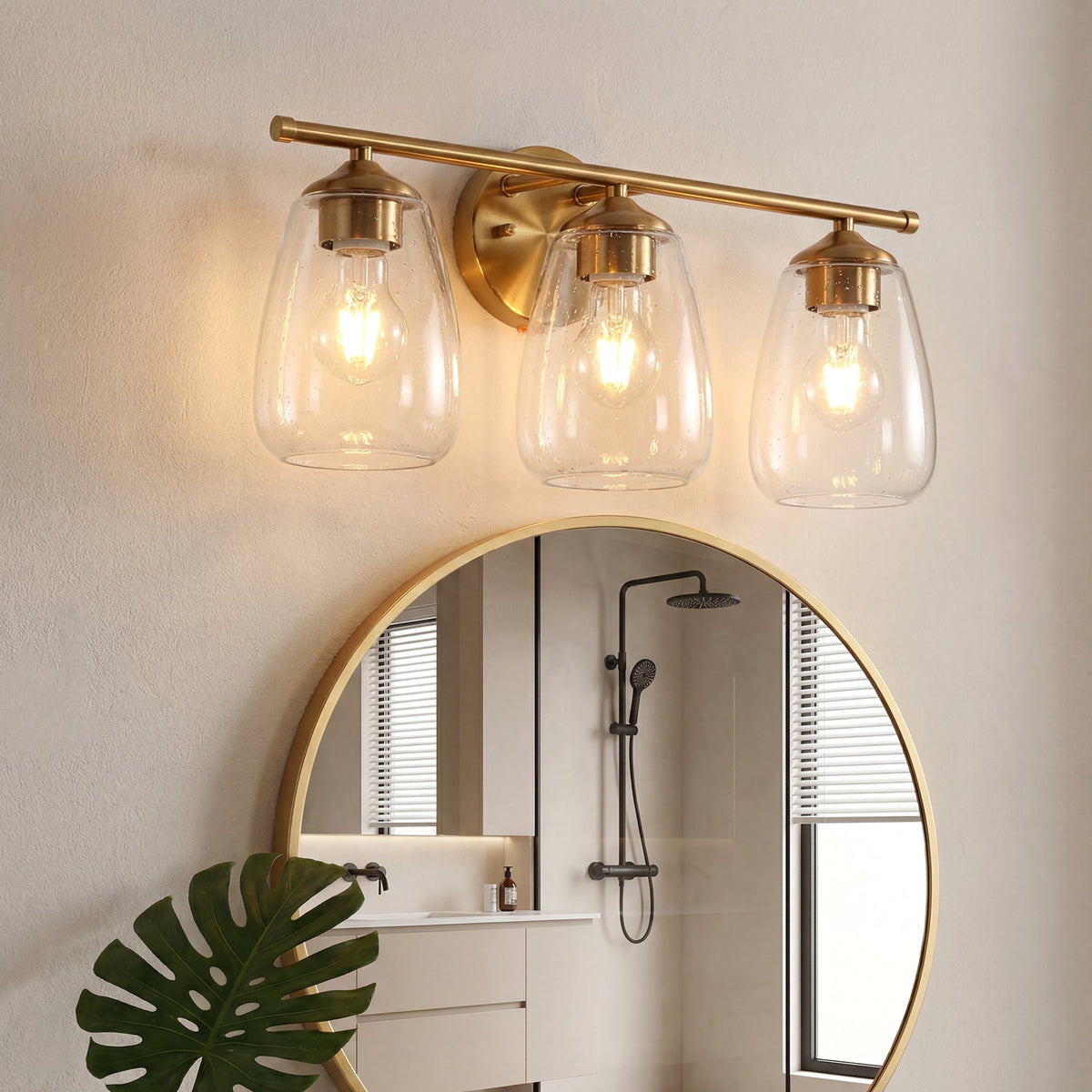 Gold bathroom vanity light with three bubble glass shades, shown mounted above a round mirror in a bathroom