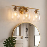 Gold bathroom vanity light with three bubble glass shades, shown mounted above a round mirror in a bathroom