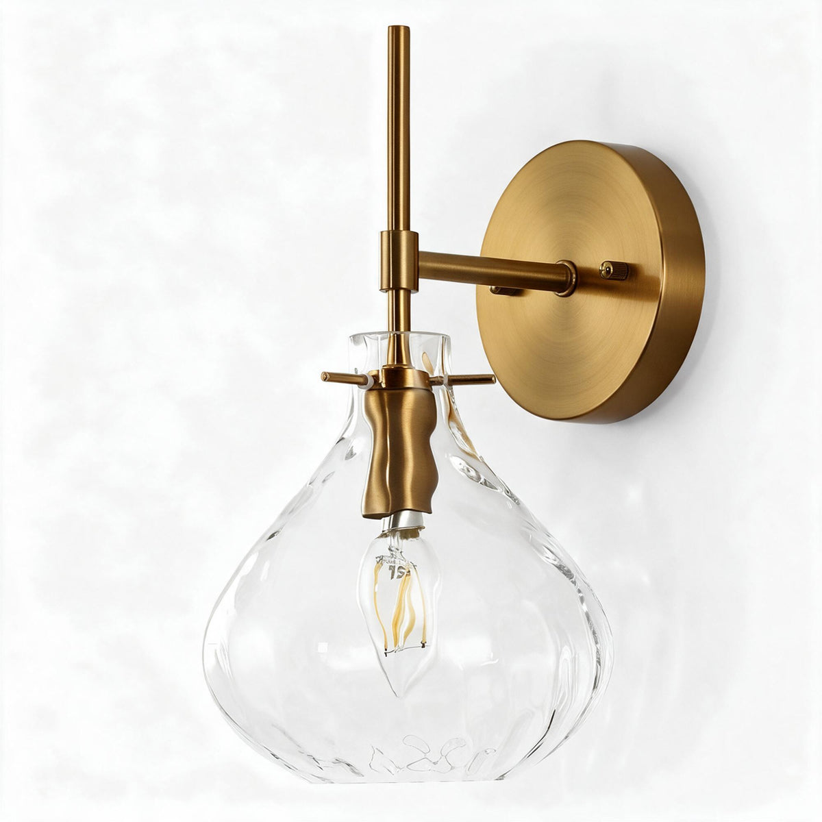 Gold wall sconce with clear hammered glass shade and exposed bulb, shown at an angle