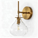 Gold wall sconce with clear hammered glass shade and exposed bulb, shown at an angle