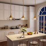 Three gold pendant lights with clear glass shades hang over a kitchen island at night