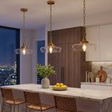 Three gold pendant lights with clear glass shades hang over a kitchen island at night
