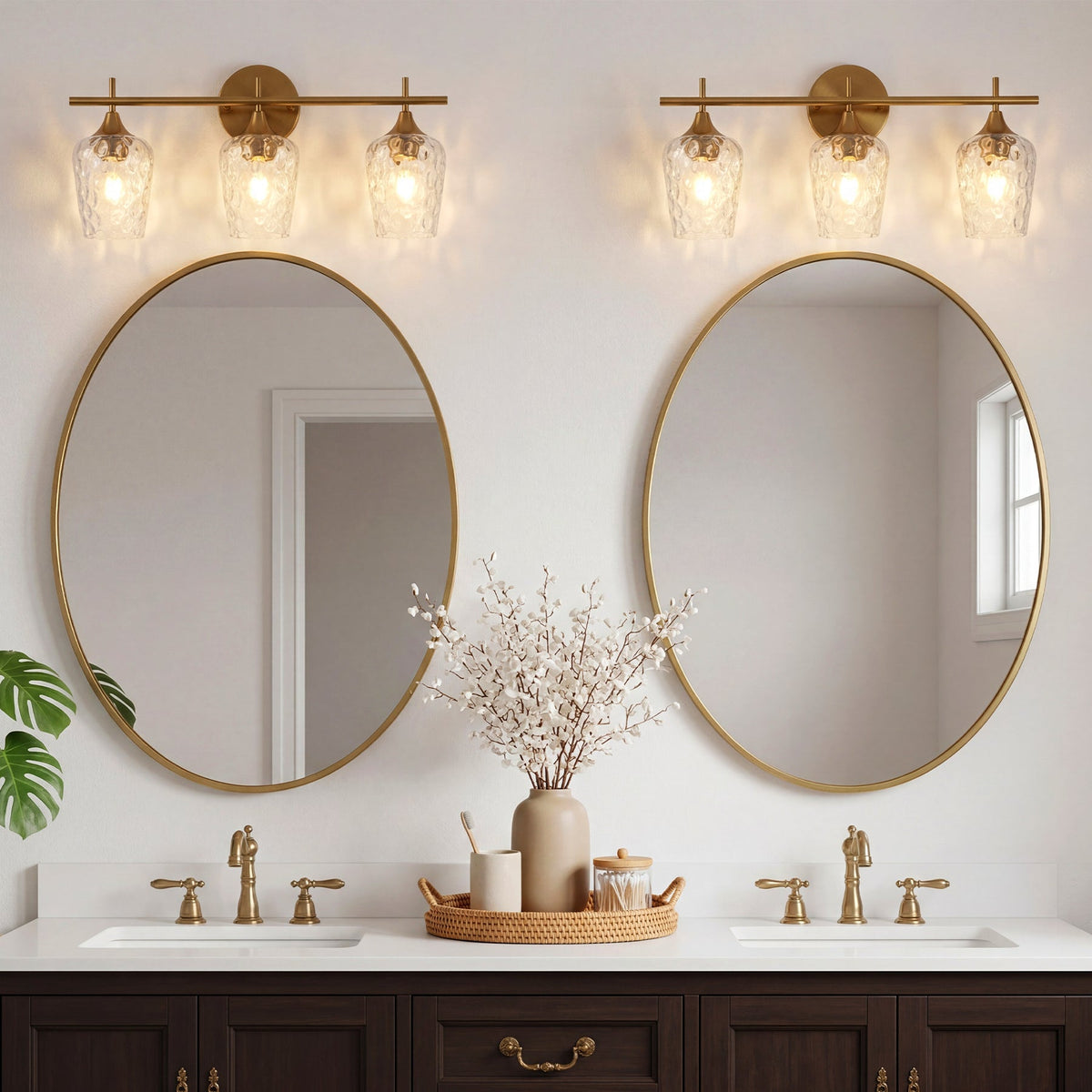 Brushed brass bathroom vanity light with three water ripple glass shades, mounted above oval mirrors in a bathroom