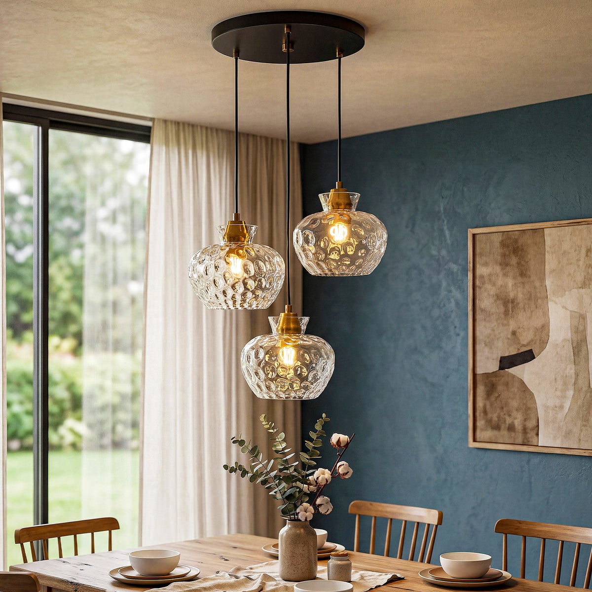 Black and gold three-light pendant with textured glass shades hanging over a wooden dining table