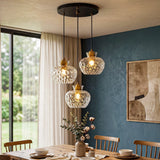 Black and gold three-light pendant with textured glass shades hanging over a wooden dining table