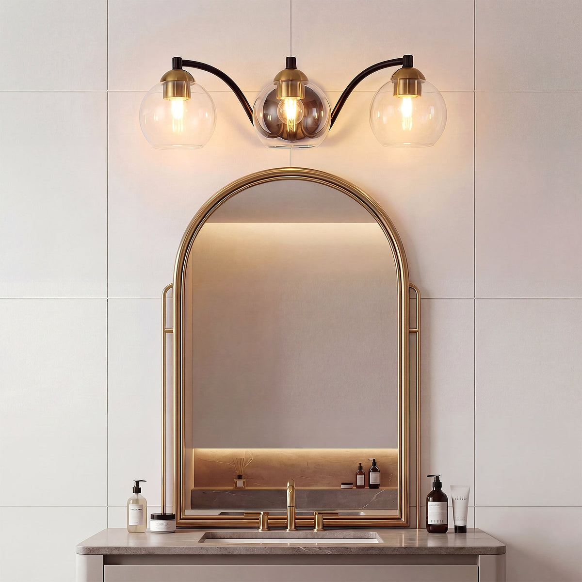 Black and brass three-light vanity fixture with clear glass globes above a bathroom mirror