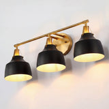Black and gold three-light vanity light with metal bell shades mounted on wall