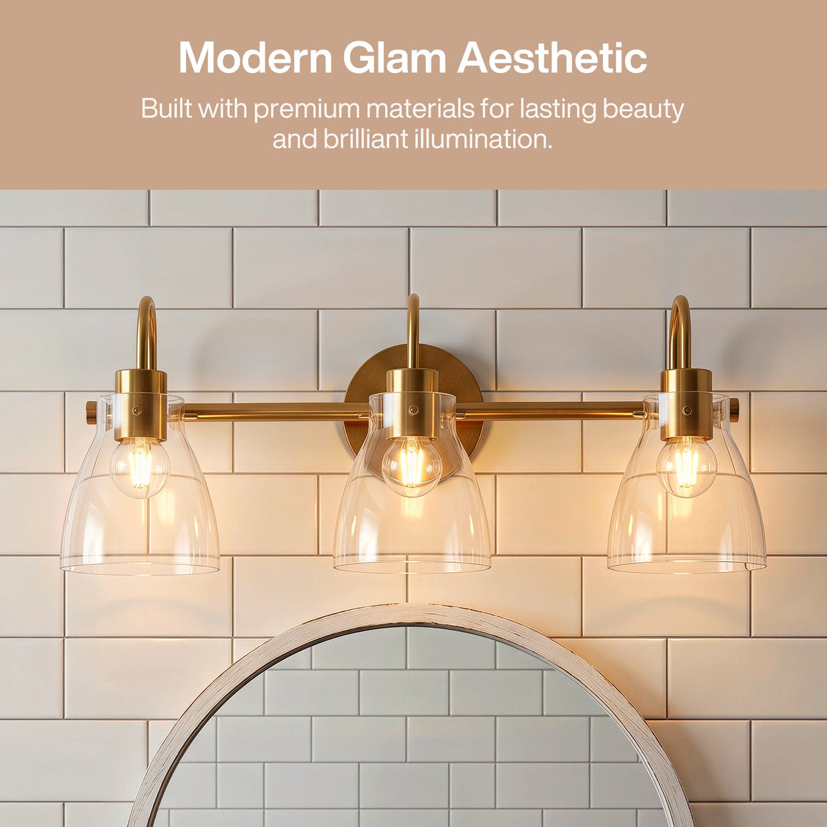 Three-light brushed brass vanity light with clear glass shades mounted above a mirror in a tiled bathroom