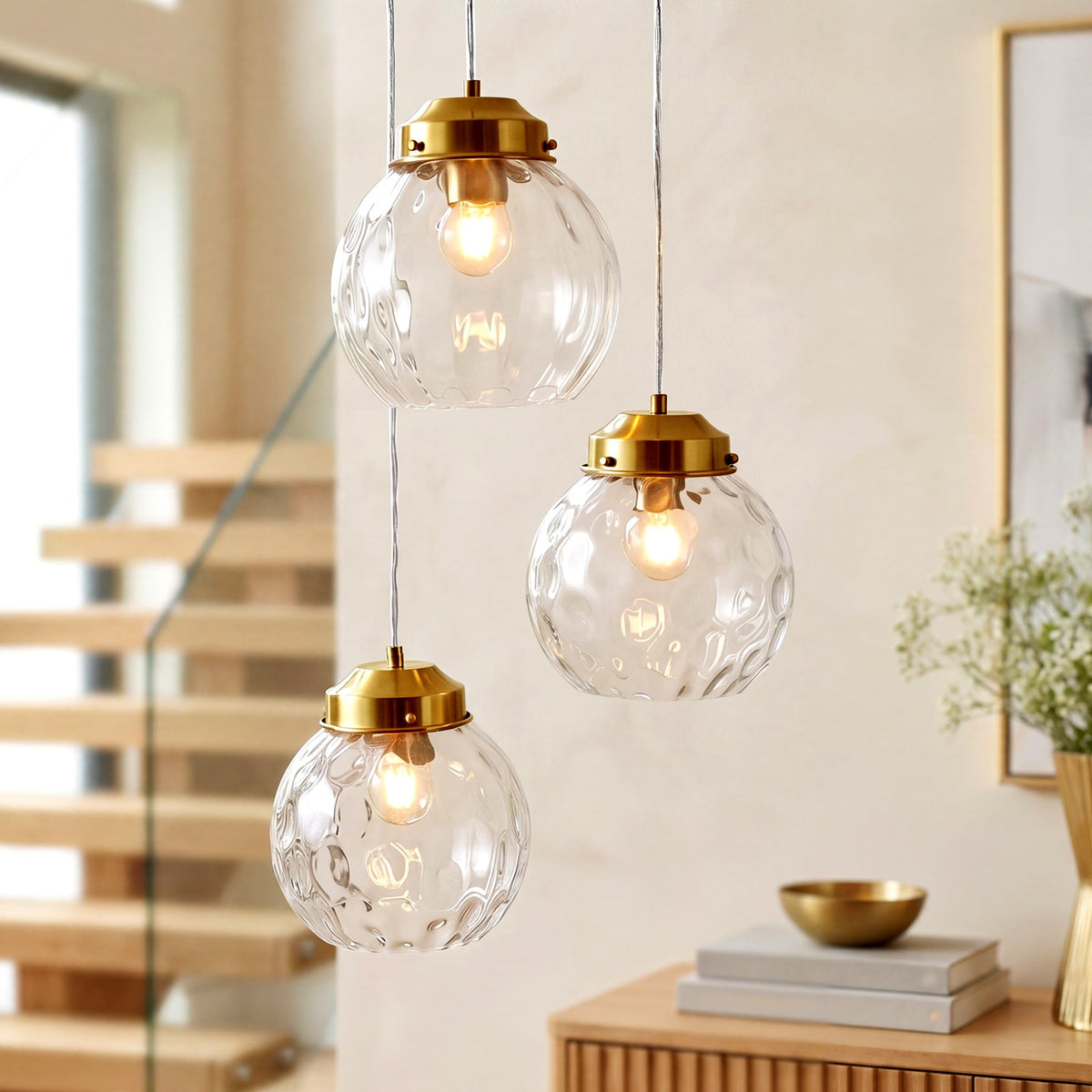 Three brushed brass pendant lights with hammered glass shades hanging in a modern room with wooden stairs