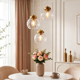 Three brushed brass pendant lights with hammered glass shades hang over a dining table