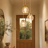 Three brushed brass pendant lights with hammered glass shades hang above a wooden door in a hallway