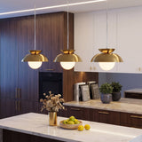 Three brass dome pendant lights with milk glass globes hang over a kitchen island