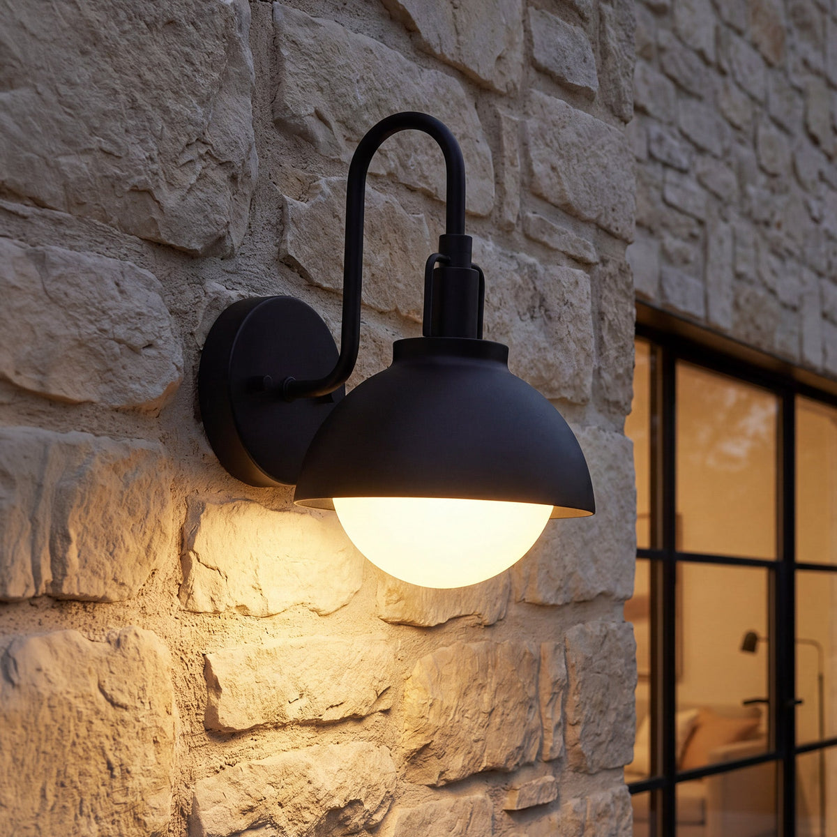 Black outdoor wall lantern with frosted glass shade mounted on stone wall, lit from within