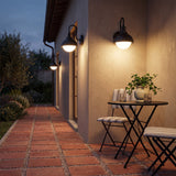 Black outdoor wall lantern with frosted glass, mounted on beige wall beside patio table