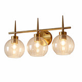 Three-light vanity light with brushed brass finish and clear glass globe shades, shown from front angle