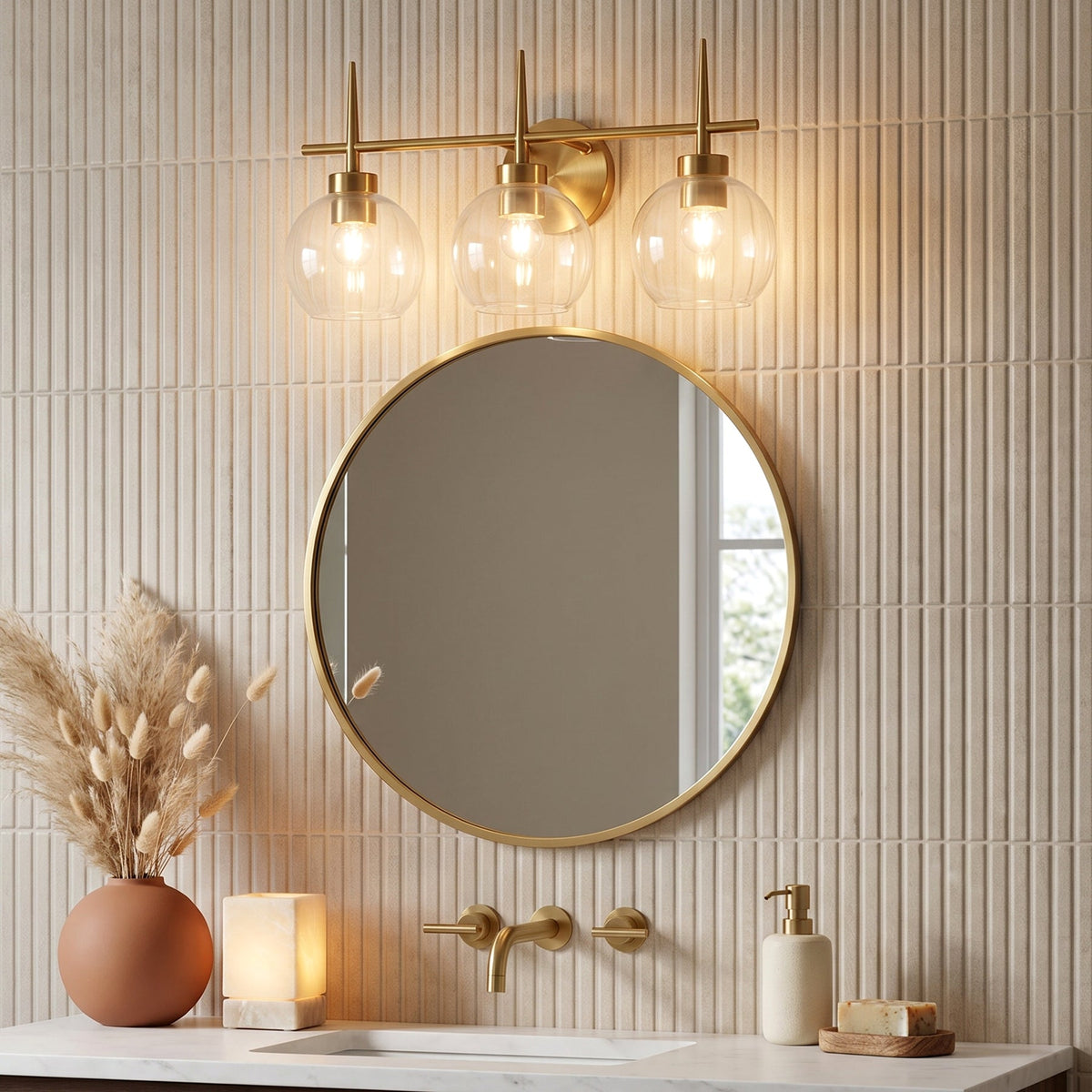 Brushed brass three-light vanity fixture with clear globe shades above a round mirror in a bathroom