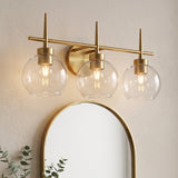 Three-light brushed brass vanity light with clear globe shades mounted above a mirror