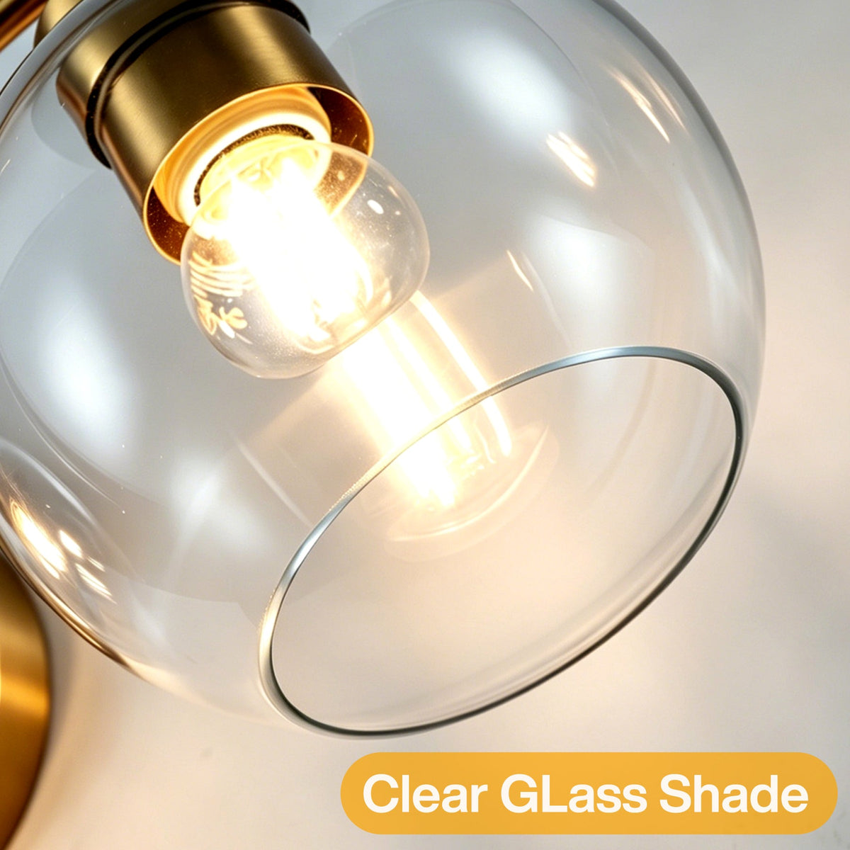 Close-up of a brushed brass bathroom vanity light with a clear glass globe shade and lit bulb