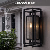 Black outdoor wall sconce with seeded glass, shown lit and raining, mounted on a wall
