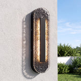 Black oval LED outdoor wall sconce with textured glass, mounted on a light-colored wall